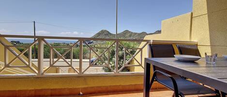 An outdoor terrace with a table and chairs, a view of a mountain, and a yellow wall.