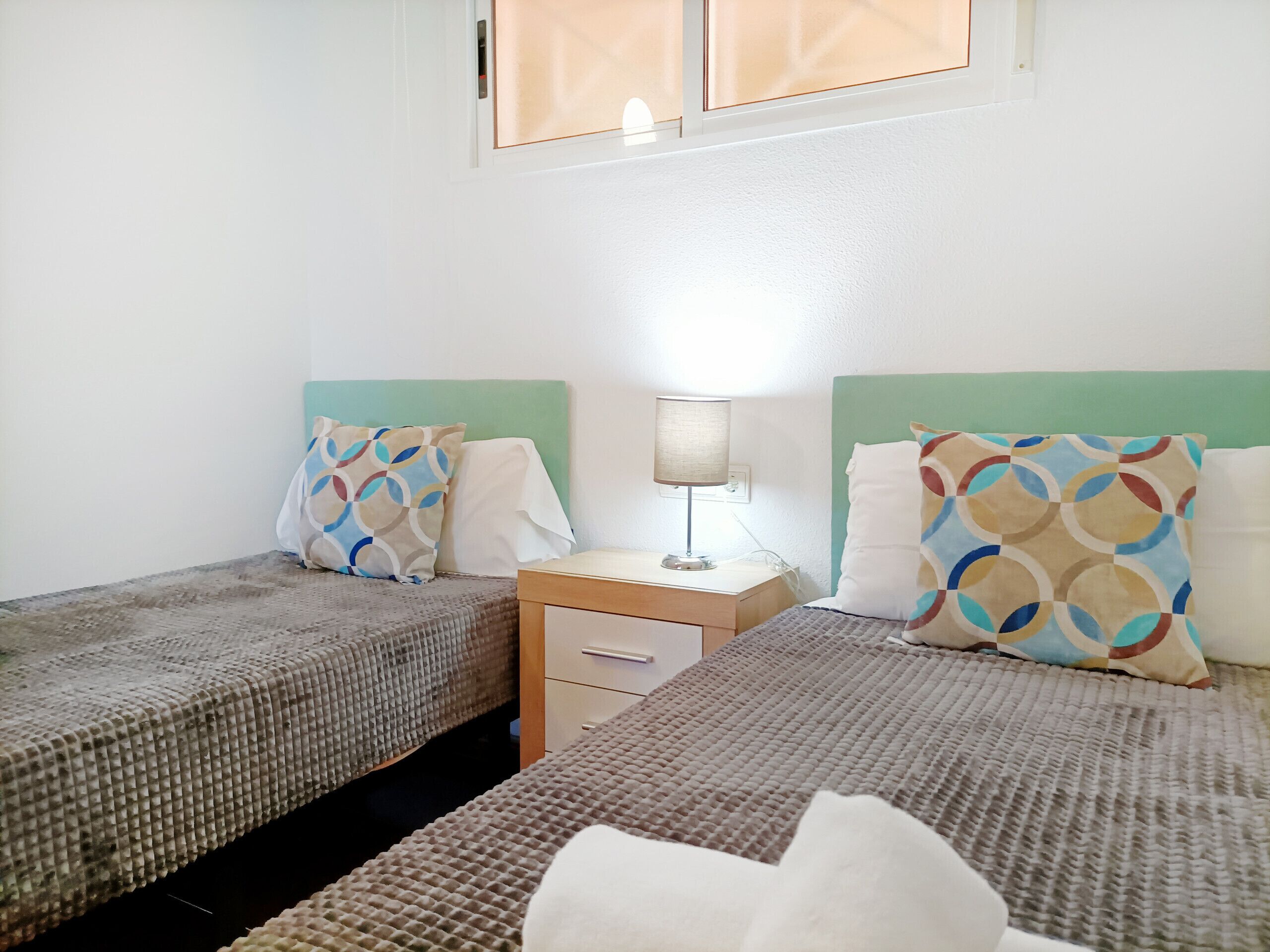 Een tweepersoonskamer met twee bedden, een nachtkastje met een lamp en een klein dressoir.