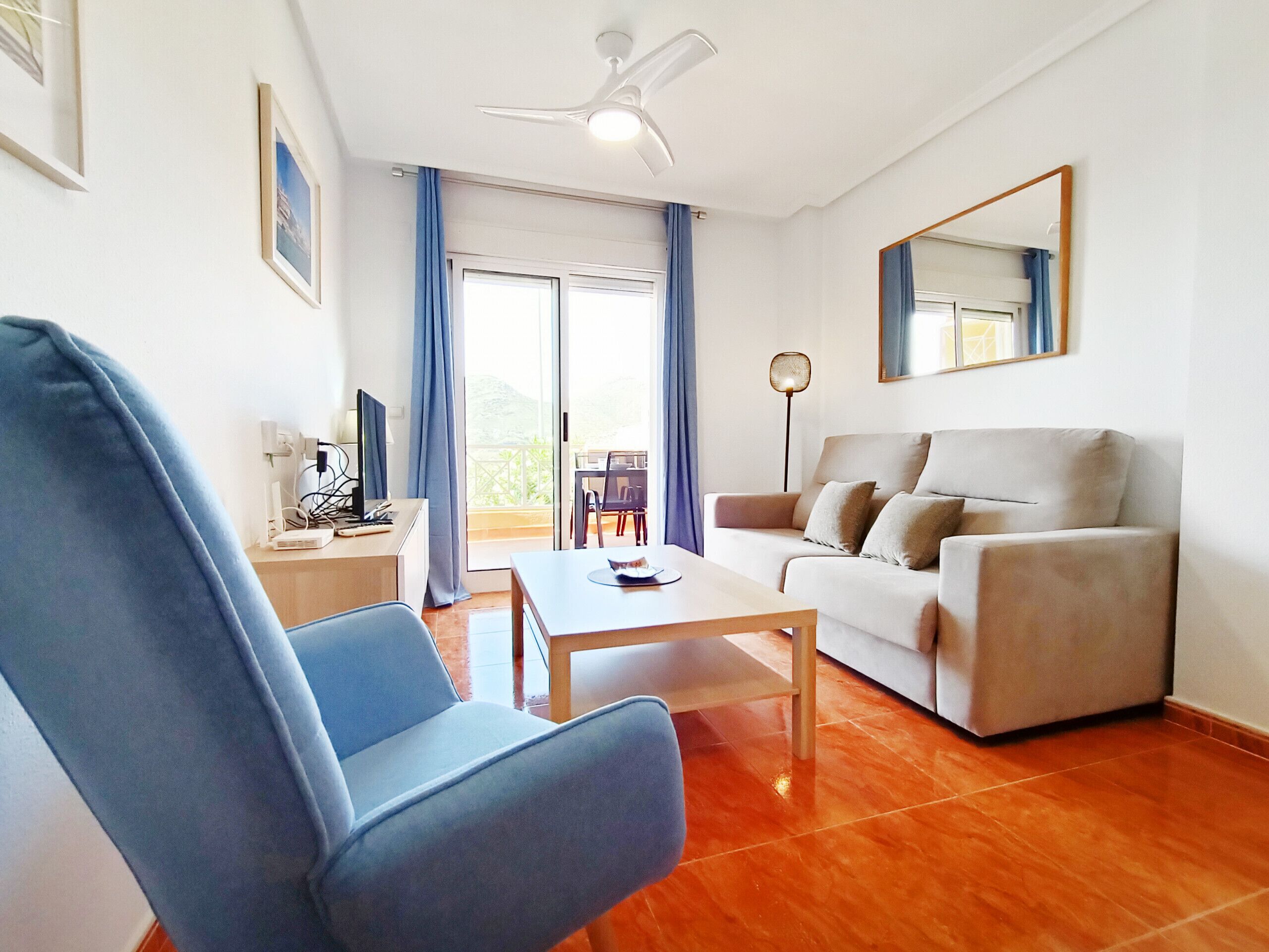 A modern living room with a blue armchair, a beige sofa, a wooden coffee table, and a ceiling fan.