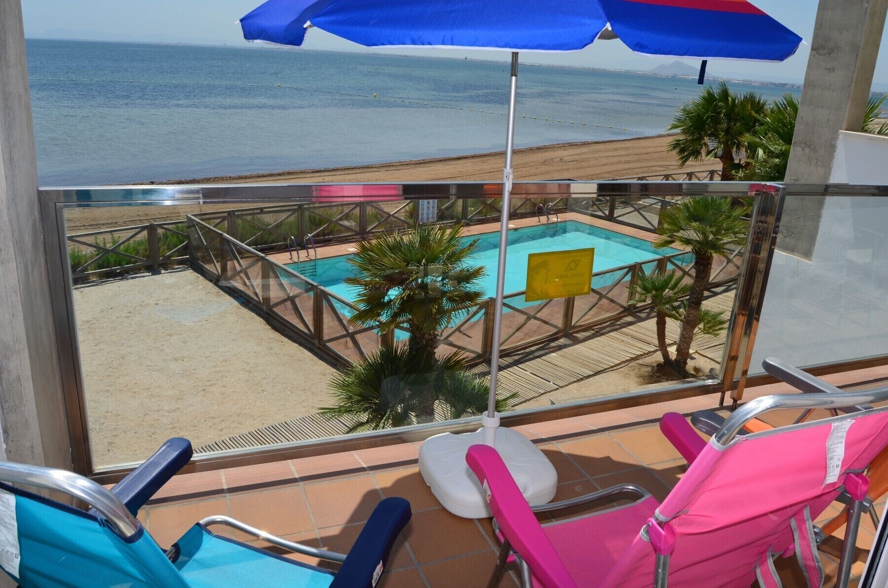 Een balkon met zwembad, uitzicht op het strand en ligbedden.