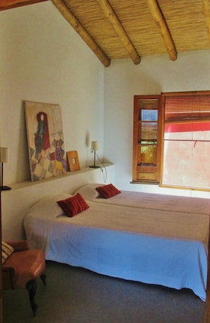 Un dormitorio con una cama grande, techo de madera, un cuadro en la pared y una ventana con persianas.