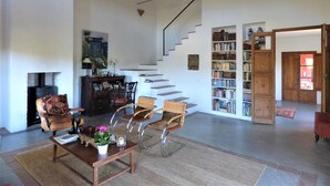 Een ruime woonkamer met een open haard, een trap en een grote boekenkast.