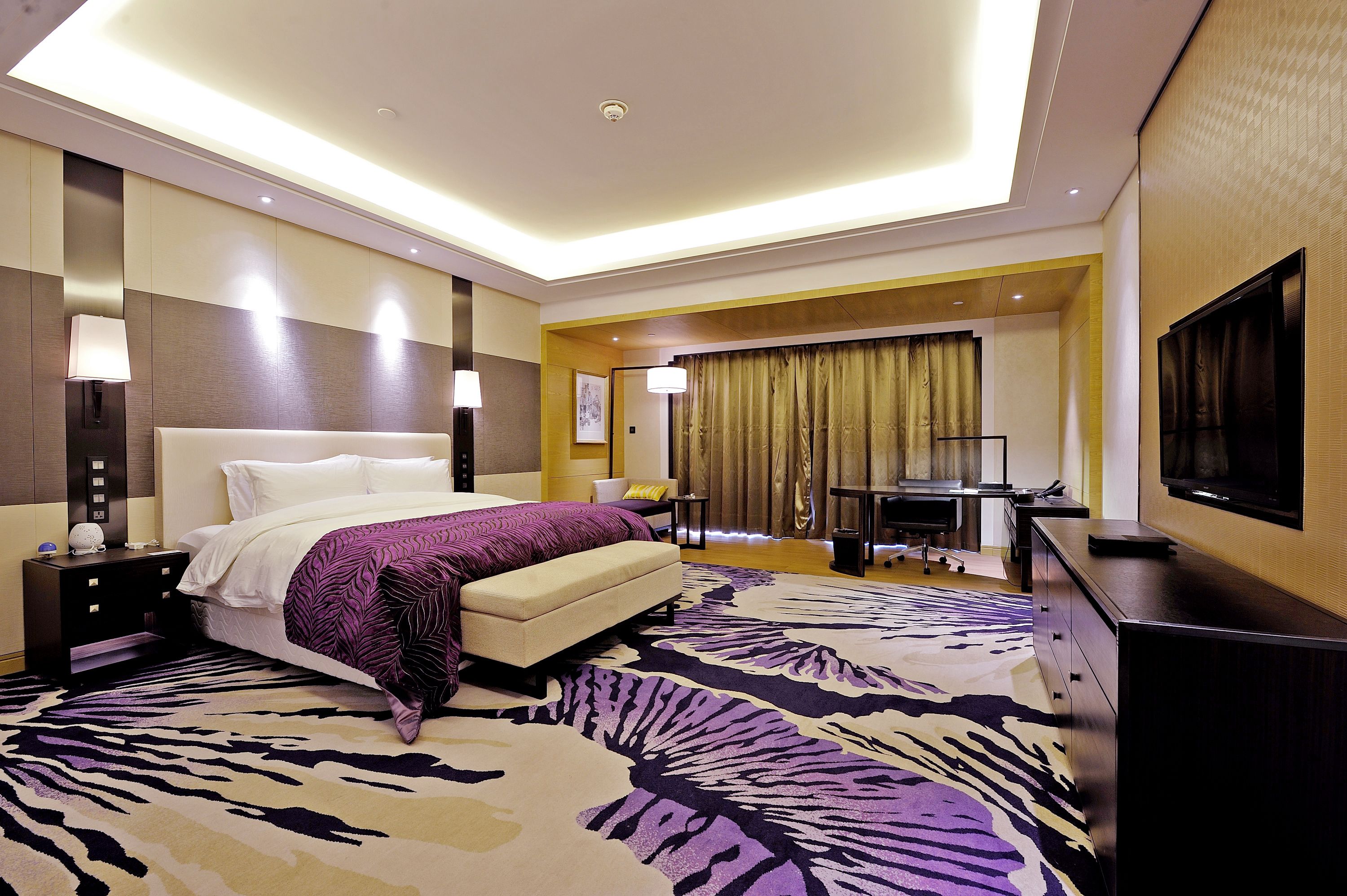 A hotel room with a large bed, a desk, a television, and a zebra-patterned carpet.