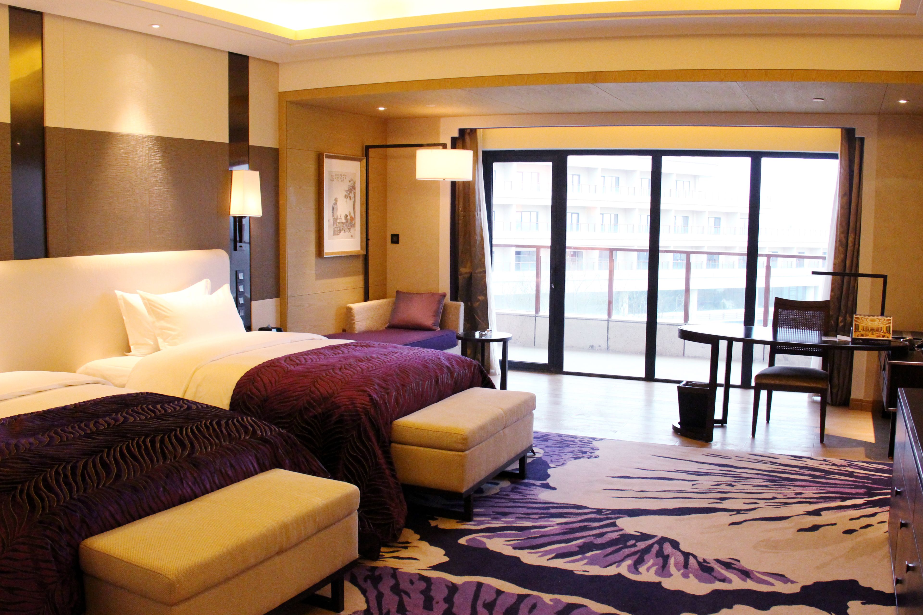 Een hotelkamer met een groot bed, een bank, een bureau en uitzicht op de stad.