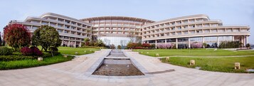 Un edificio moderno con fachada curva, una fuente central y jardines bien cuidados.