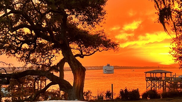 A pool area with a sunset view, a dock, and a boat in the distance.