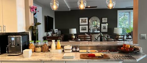 Una cocina moderna con una isla central, electrodomésticos de acero inoxidable y una zona de comedor con pared oscura y fotografías enmarcadas.
