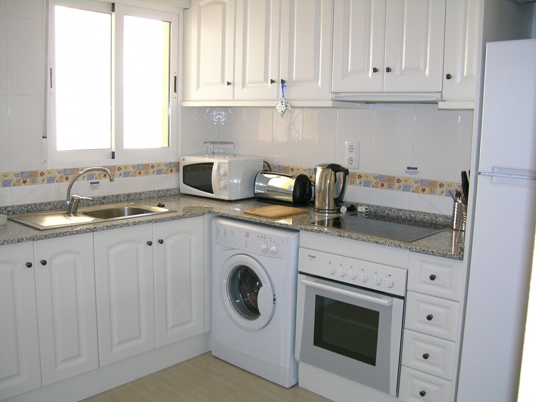 A compact kitchen with white cabinets, a washing machine, a microwave, a toaster, and a kettle.