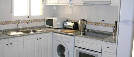 A compact kitchen with white cabinets, a washing machine, a microwave, a toaster, and a kettle.