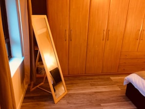 A room with wooden flooring, a bed, a wardrobe, and a standing mirror.