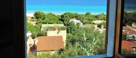 A view from a window with a curved frame, overlooking a coastal area with buildings and a clear blue sky.