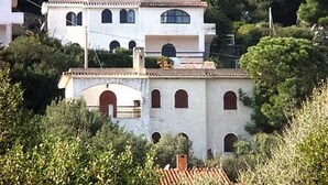 A white building with multiple arches and a red door, surrounded by greenery. - Large panoramic apartment, beautiful sea view. (Costa Rei)