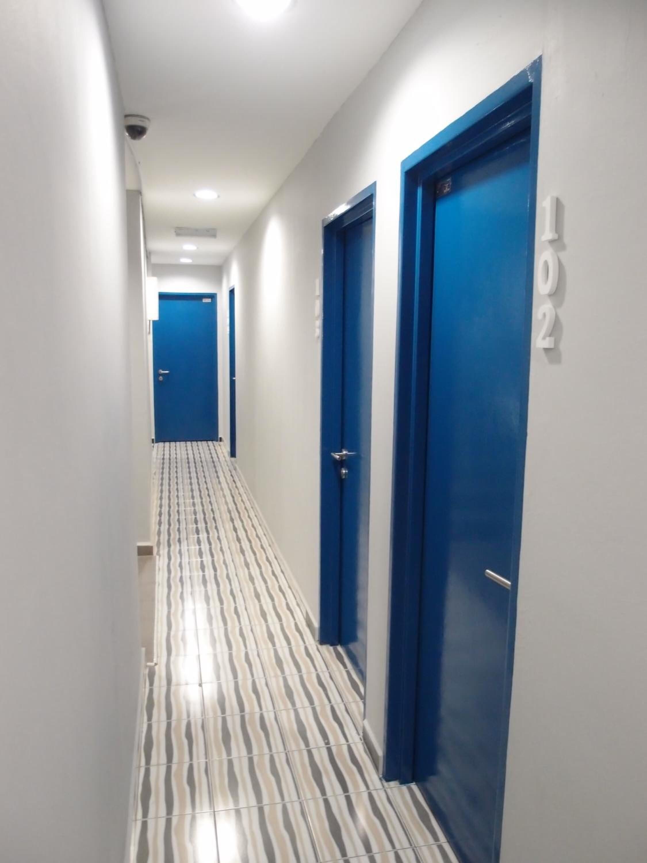 A corridor with blue doors, each marked with a number. The floor has a striped pattern.