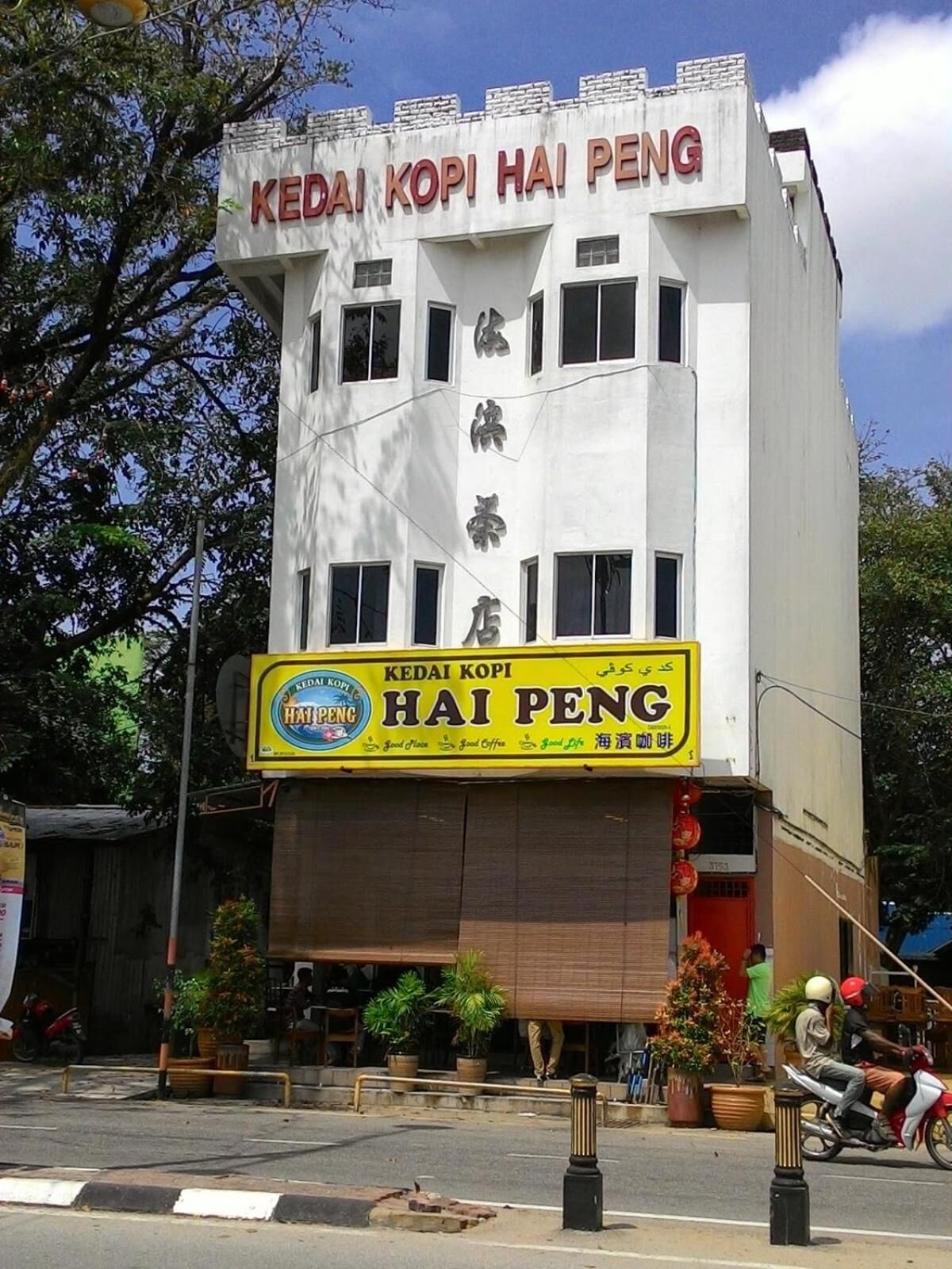 A building with a sign reading "Kedai Kopi Hai Peng" and a yellow sign below it.