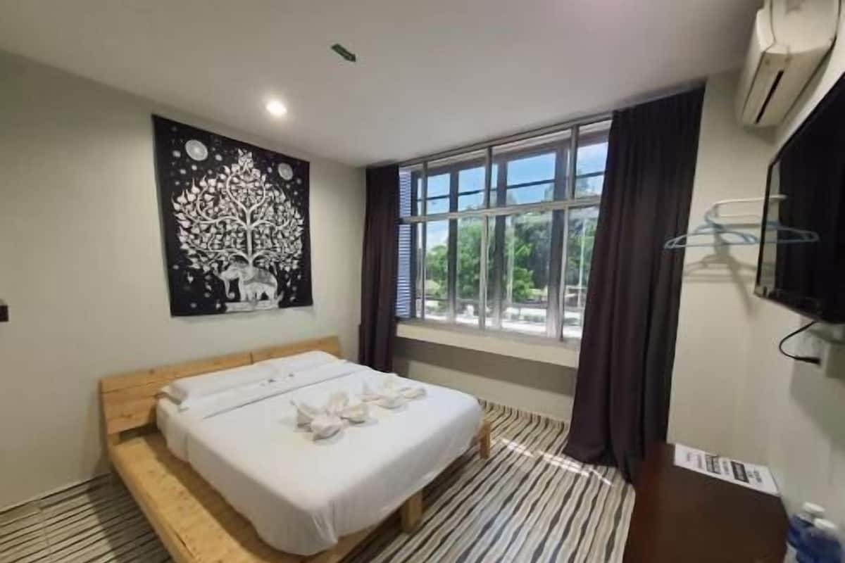 A hotel room with a bed, a window with curtains, a wall-mounted TV, and a painting.