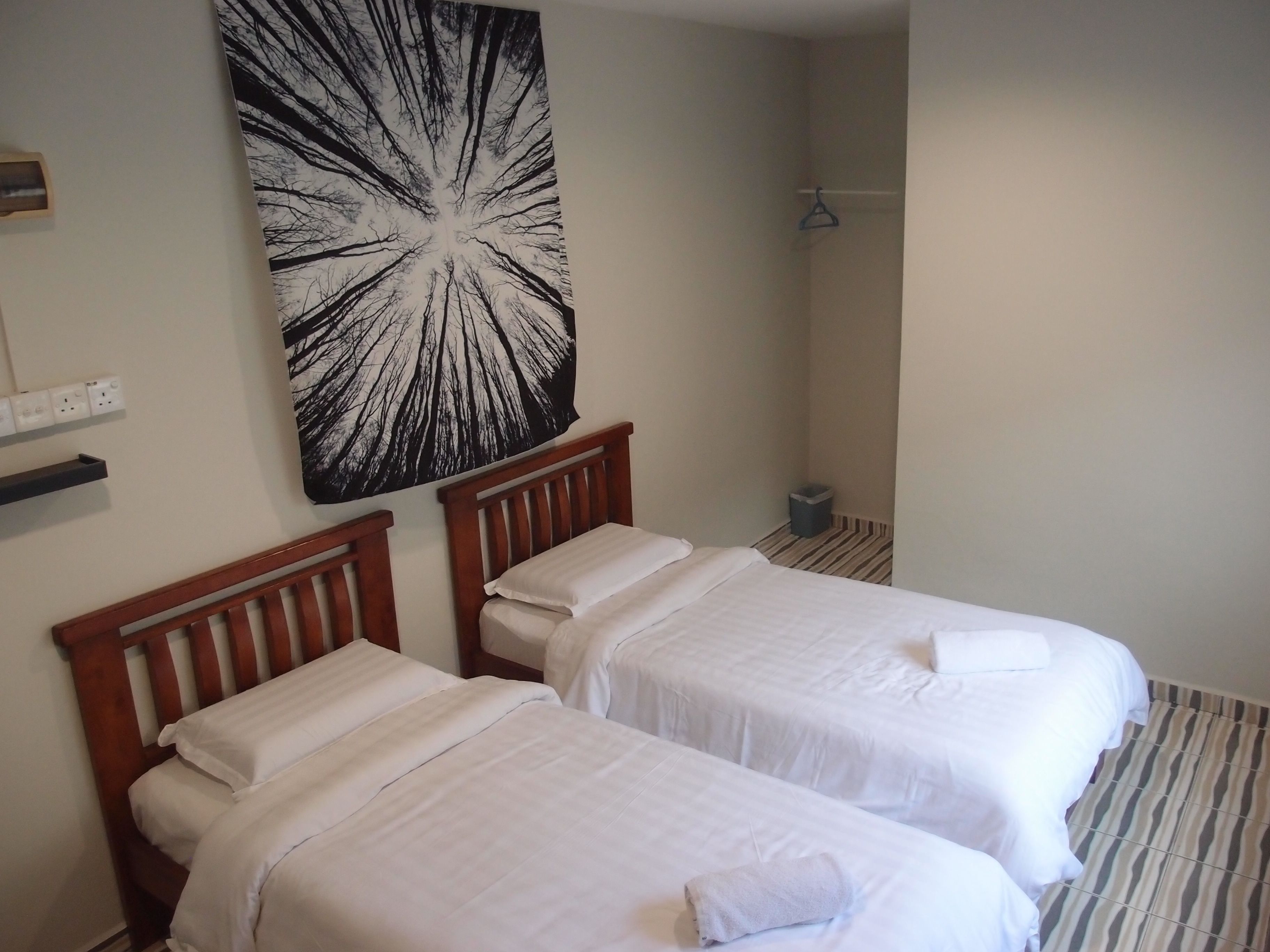 A hotel room with two single beds, a large abstract wall art, a small trash bin, and a coat hanger.
