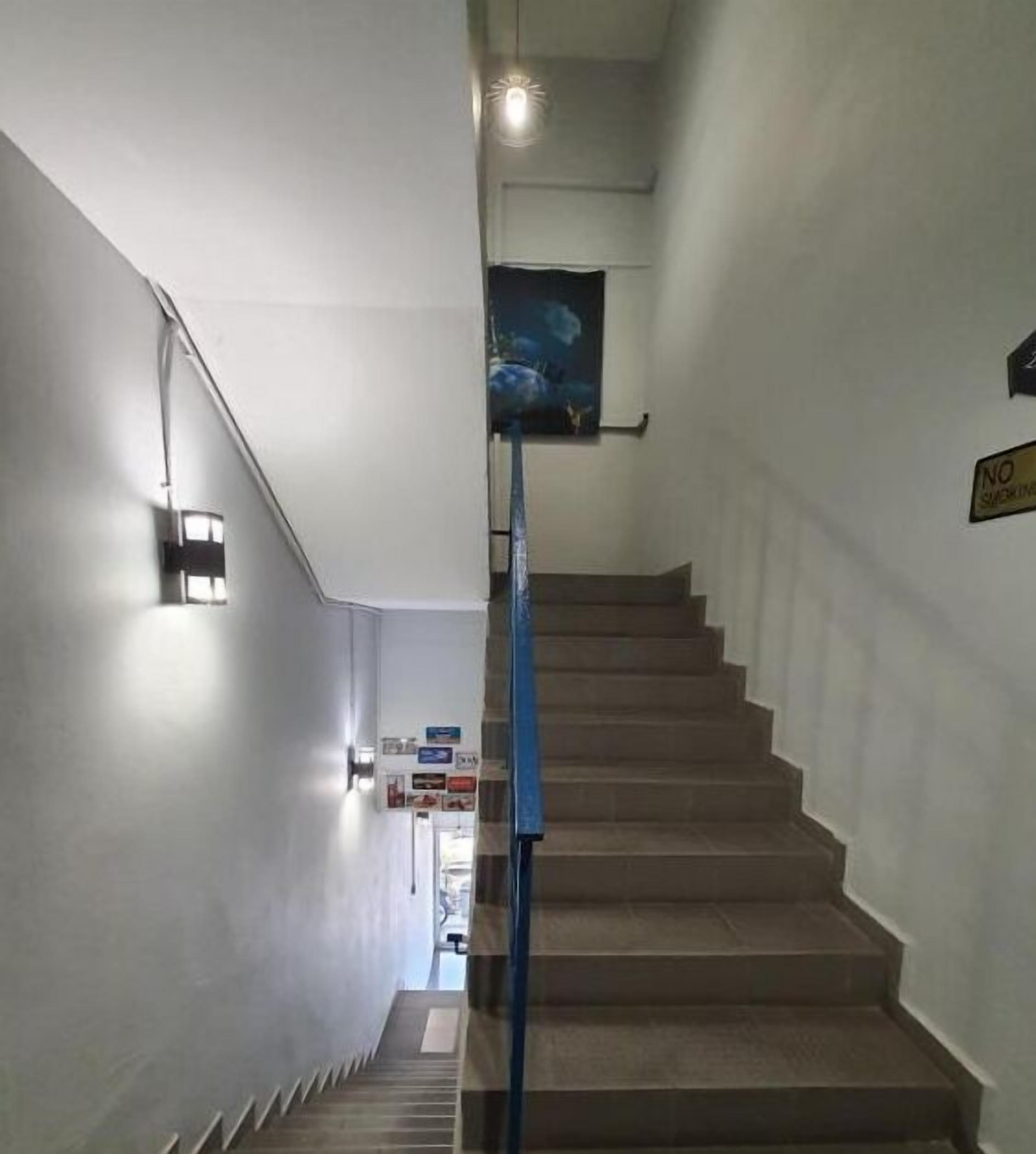 A staircase with a blue handrail, a 'NO SMOKING' sign, and a poster on the wall.