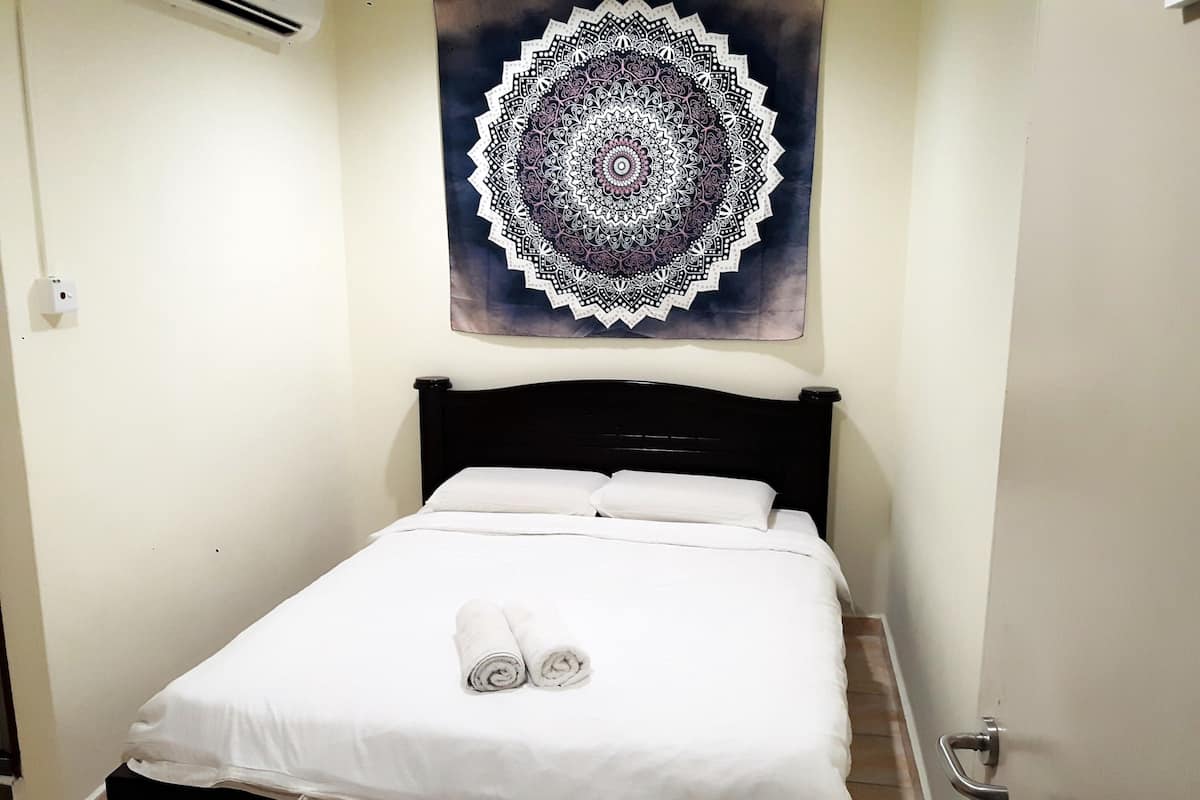 A neatly made bed with white linens and two rolled towels on the bed.
