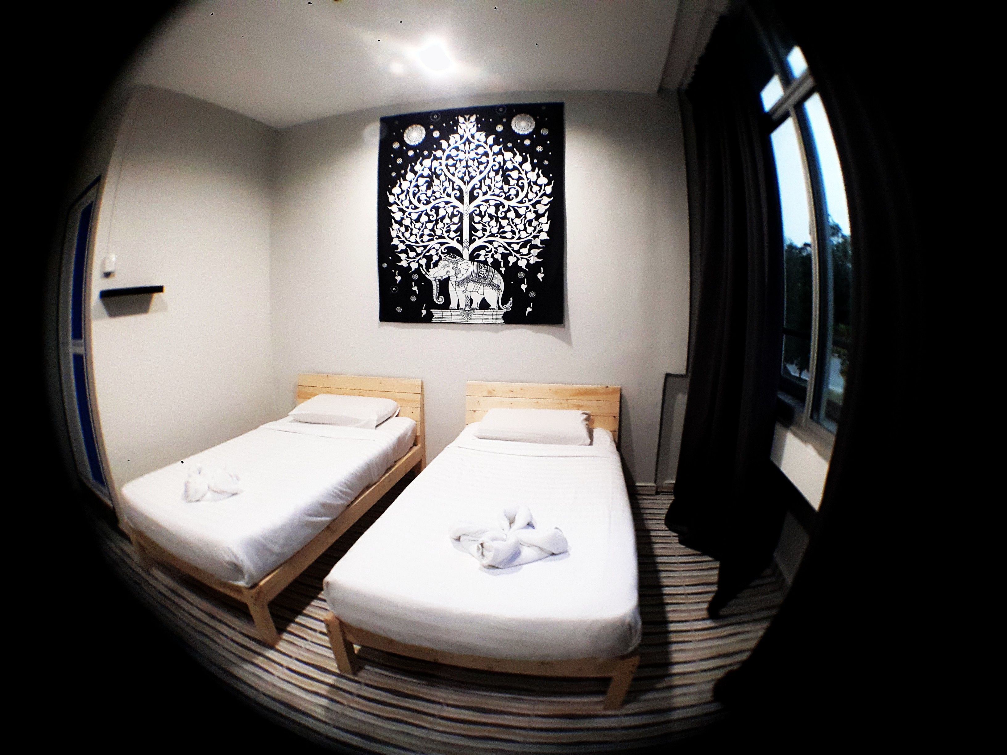 A room with two single beds, a black wall art of a tree, and a window with curtains.