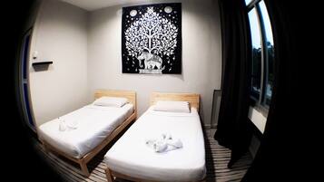 A room with two single beds, a black wall art of a tree, and a window with curtains.