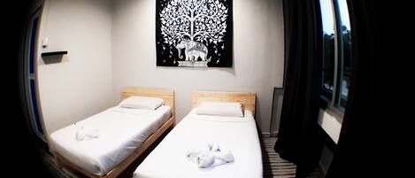 A room with two single beds, a black wall art of a tree, and a window with curtains.