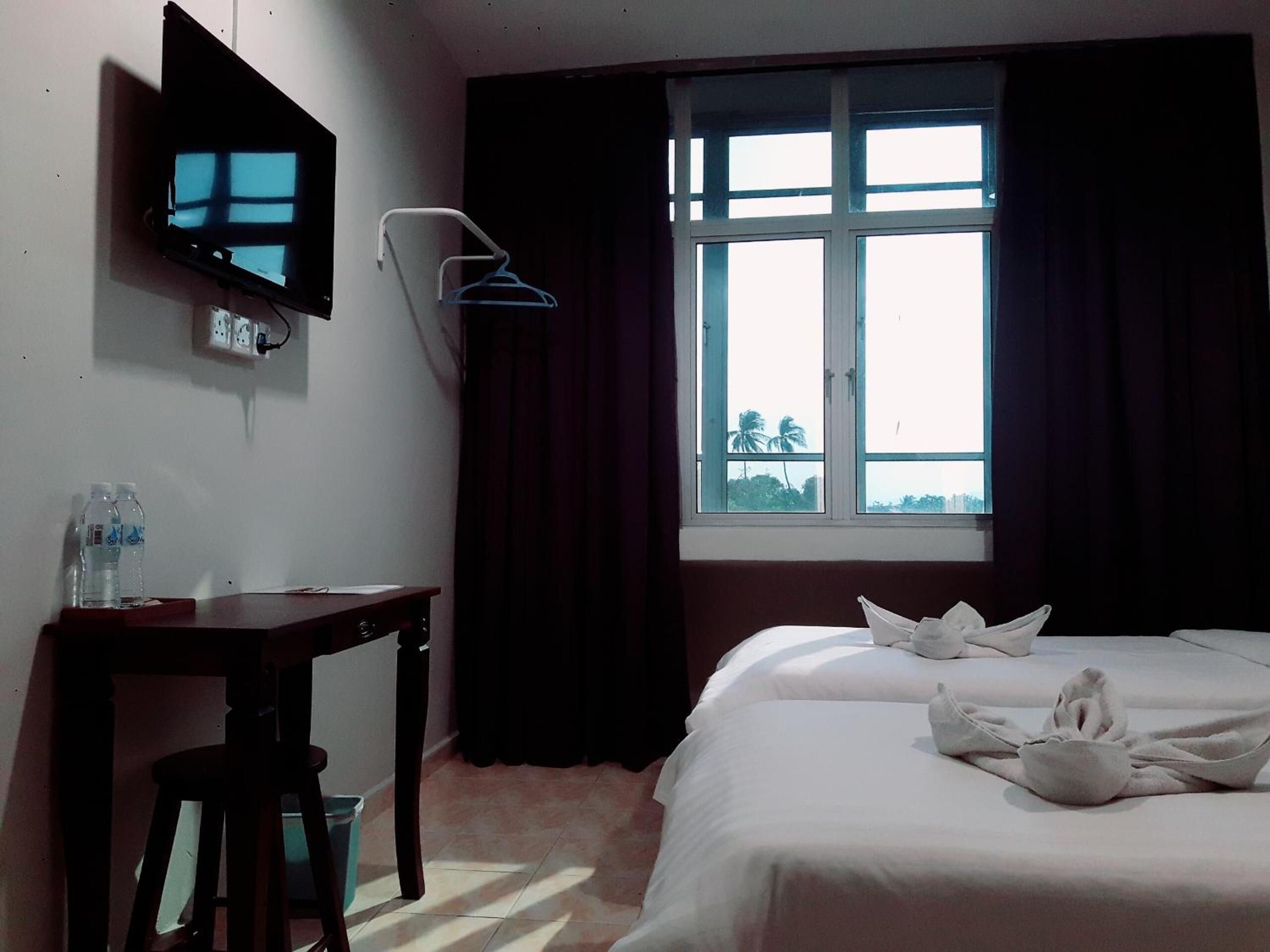 Habitación de hotel con cama, escritorio, silla, televisor montado en la pared y ventana con cortinas.