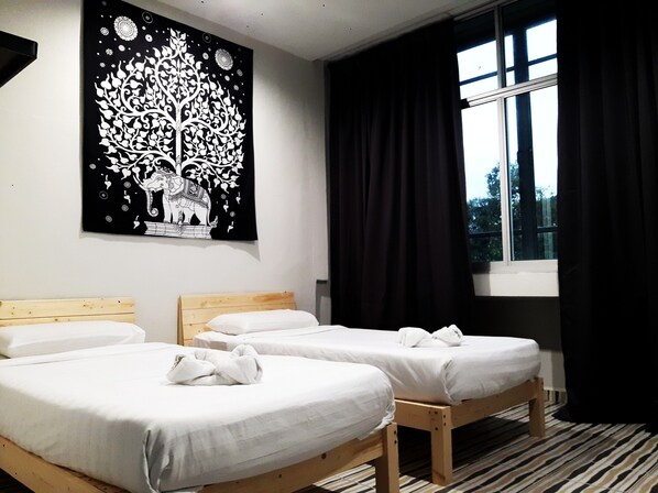 Habitación de hotel con tres camas individuales, un tapiz grande en blanco y negro, una ventana con cortinas negras y un suelo a rayas.