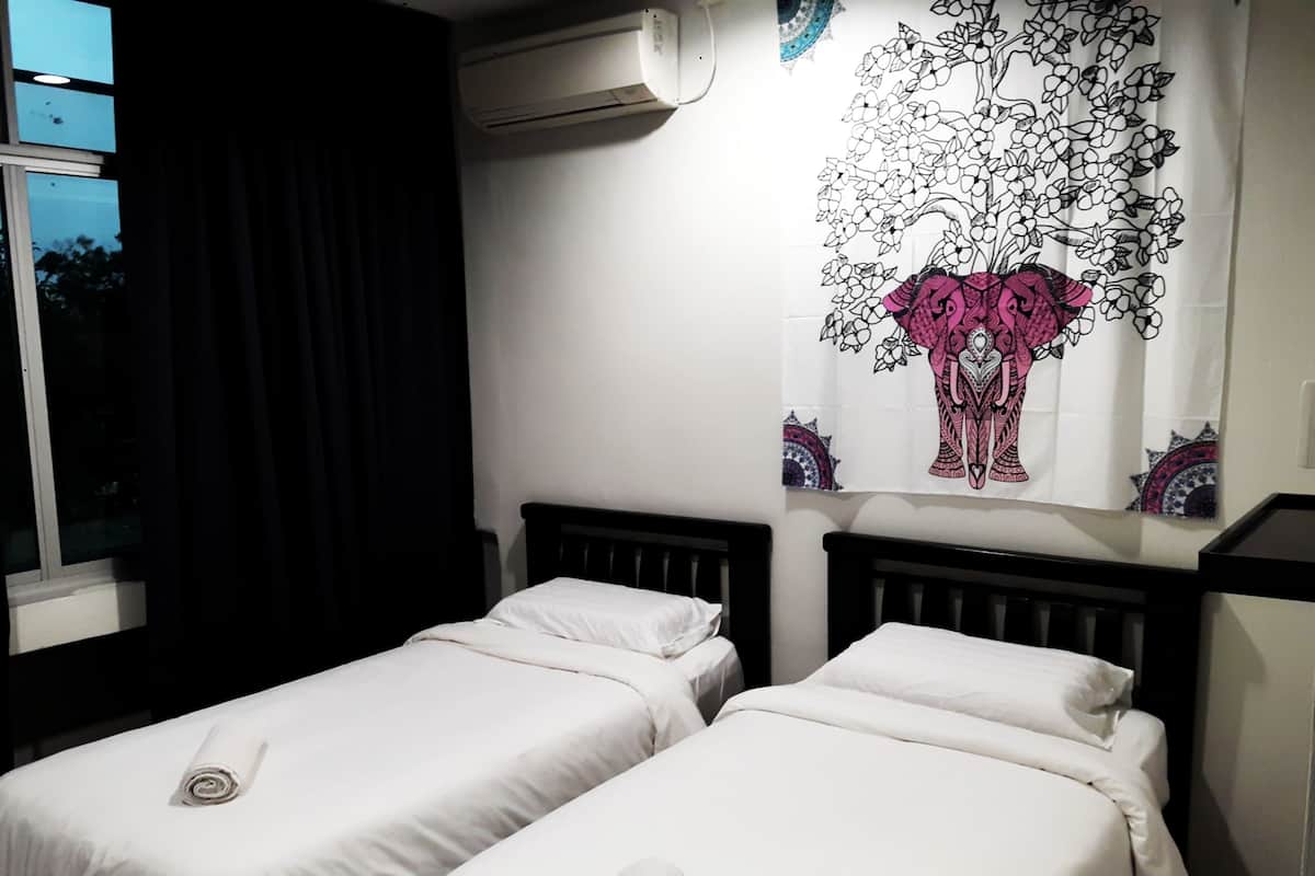 A hotel room with two single beds, a large window with curtains, an air conditioning unit, and a wall tapestry.