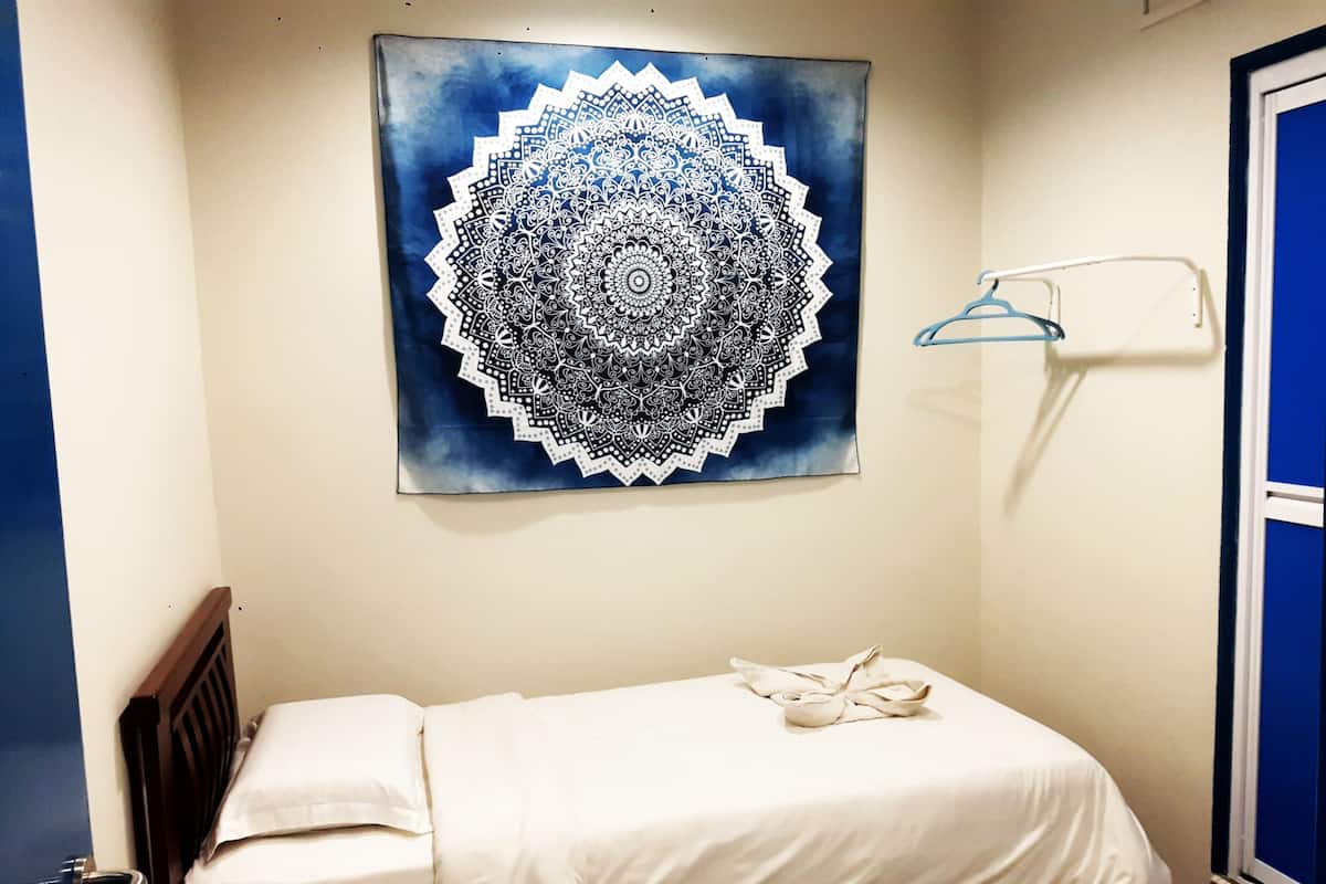 A small, neatly made bed with a white sheet and a decorative blue and white mandala artwork above it.