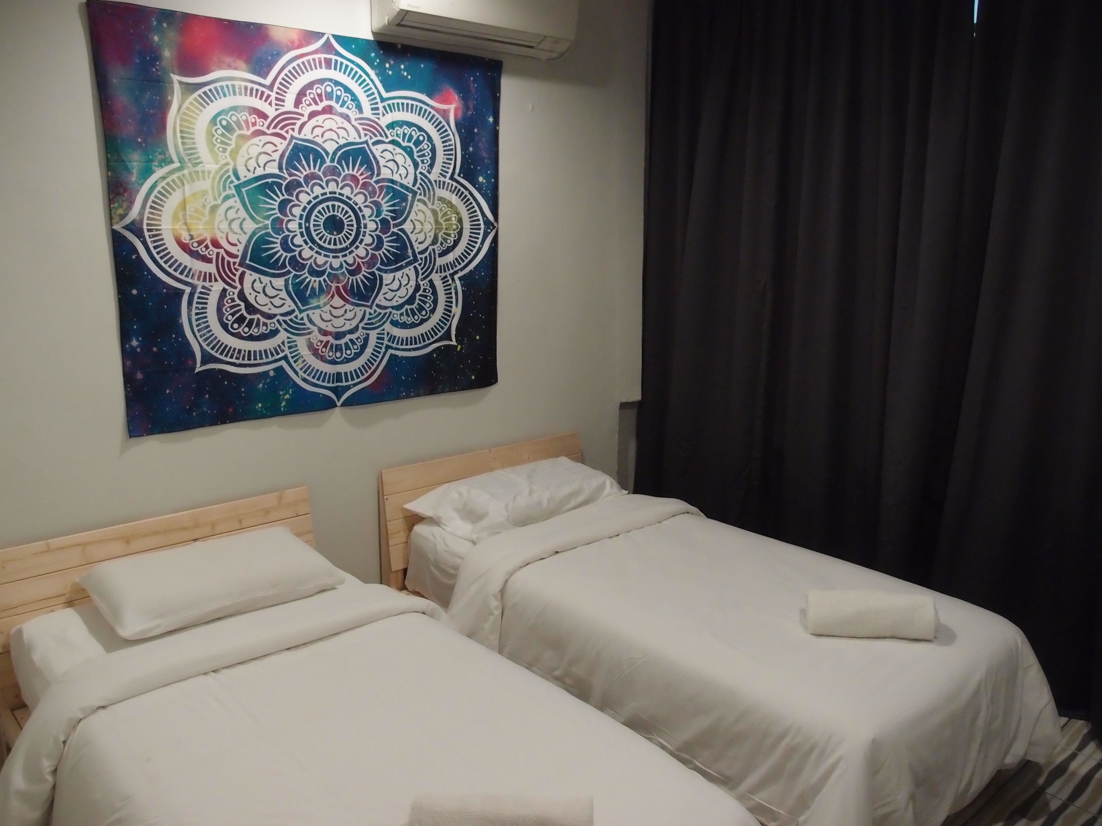 Ein Hotelzimmer mit zwei Einzelbetten, einer großen Wandteppich und einem dunklen Vorhang.