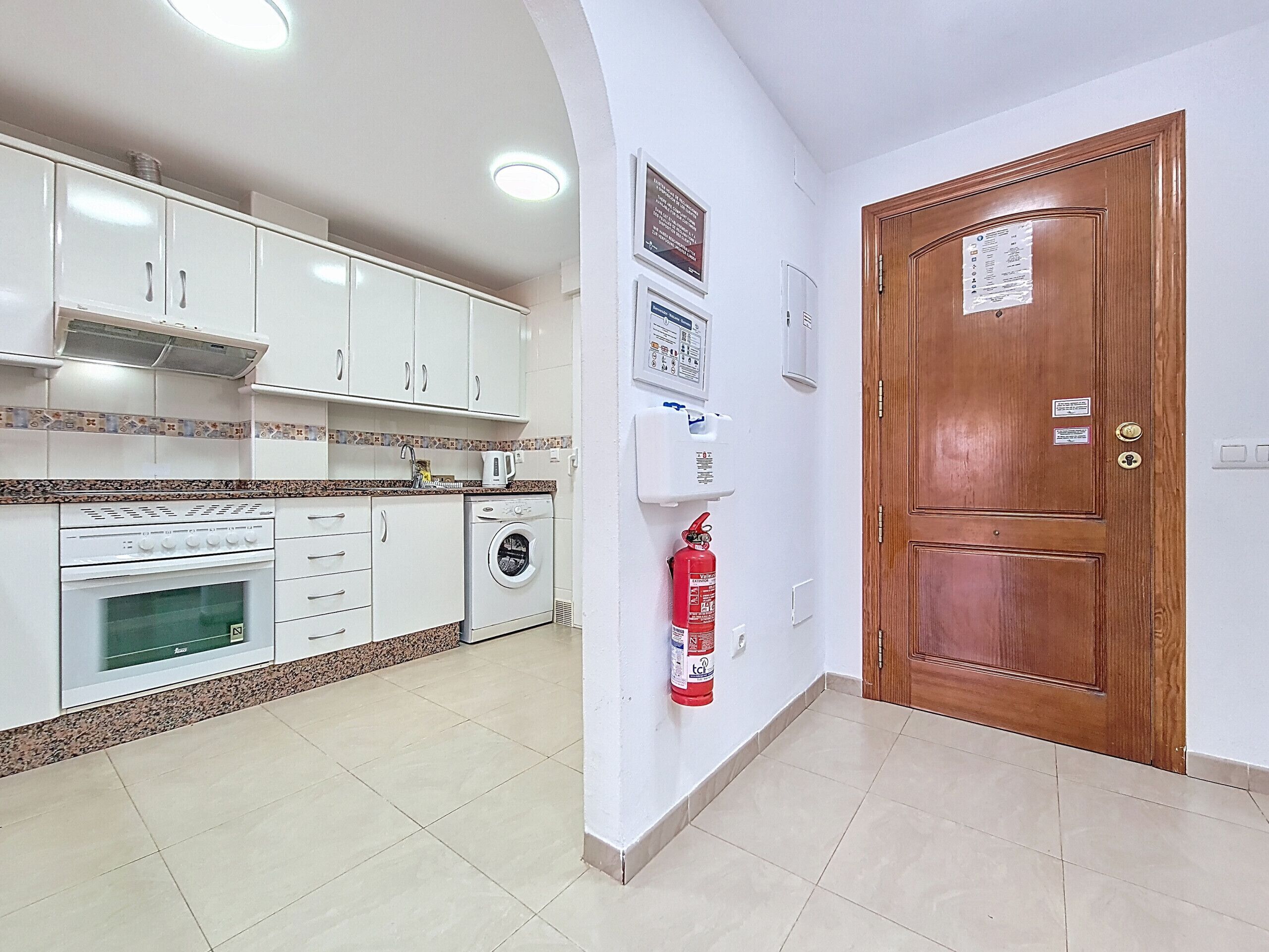 A kitchen with white cabinets, a washing machine, a coffee maker, and a fire extinguisher.
