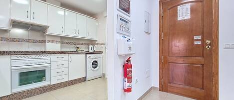 A kitchen with white cabinets, a washing machine, a coffee maker, and a fire extinguisher.
