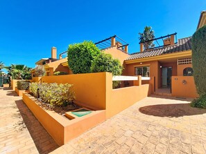 A residential building with a yellow facade, a tiled roof, and a paved courtyard.