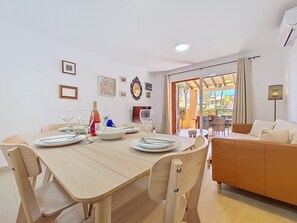 A dining area with a wooden table set for four, a sofa, and a view through a glass door to an outdoor patio.