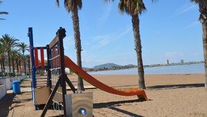 A playground with a slide on a sandy beach with palm trees and a body of water in the background.