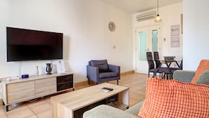 A living room with a flat-screen TV, a wooden coffee table, a grey sofa, and a red knitted throw.