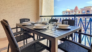 A balcony with a table set for dining, wicker chairs, and a view of buildings.