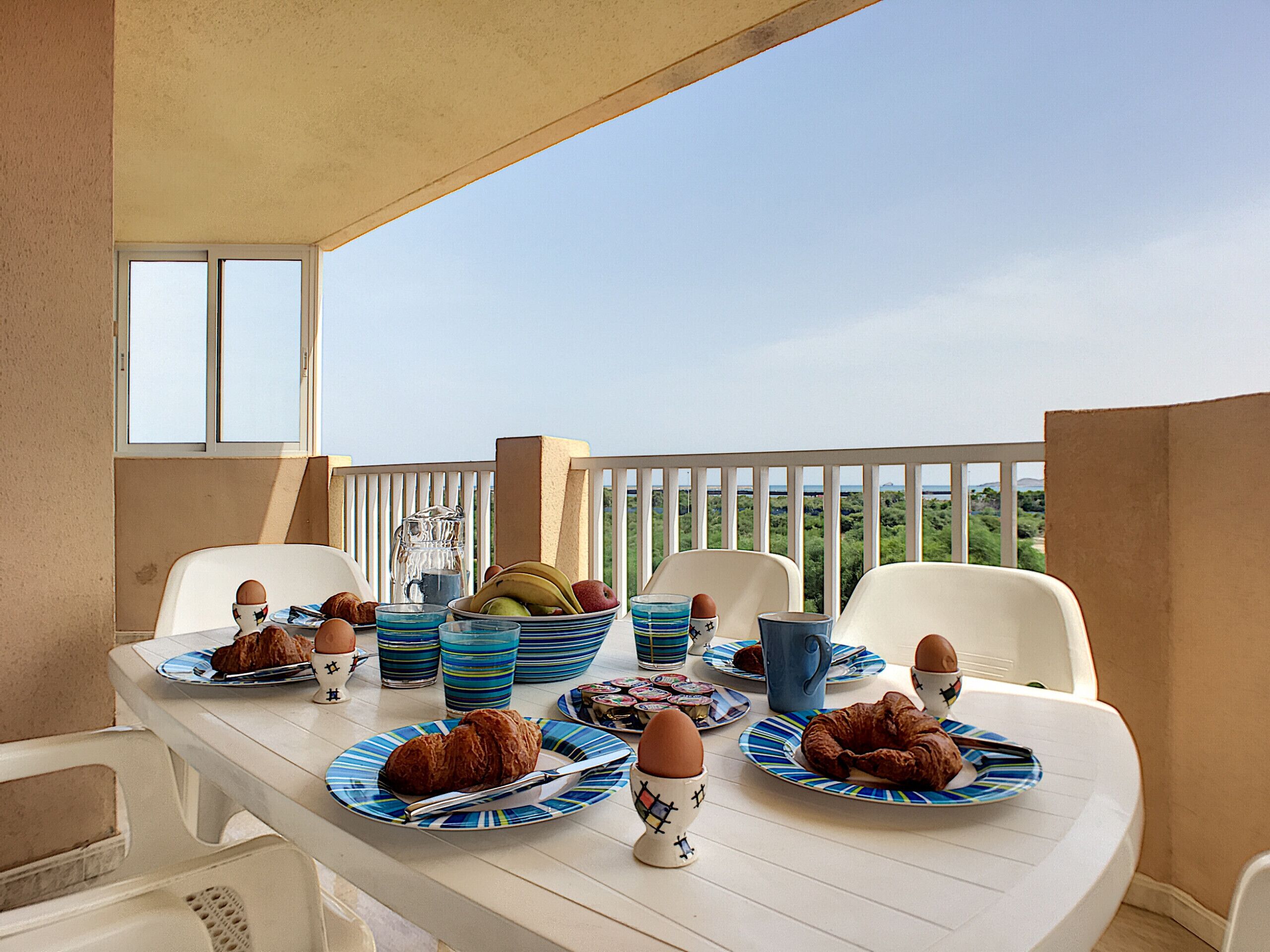 Ein Tisch für das Frühstück auf einem Balkon mit Stühlen, Tellern voller Essen und einer Karaffe.
