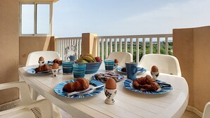 Een ontbijttafel op een balkon met stoelen, borden met eten en een karaf.