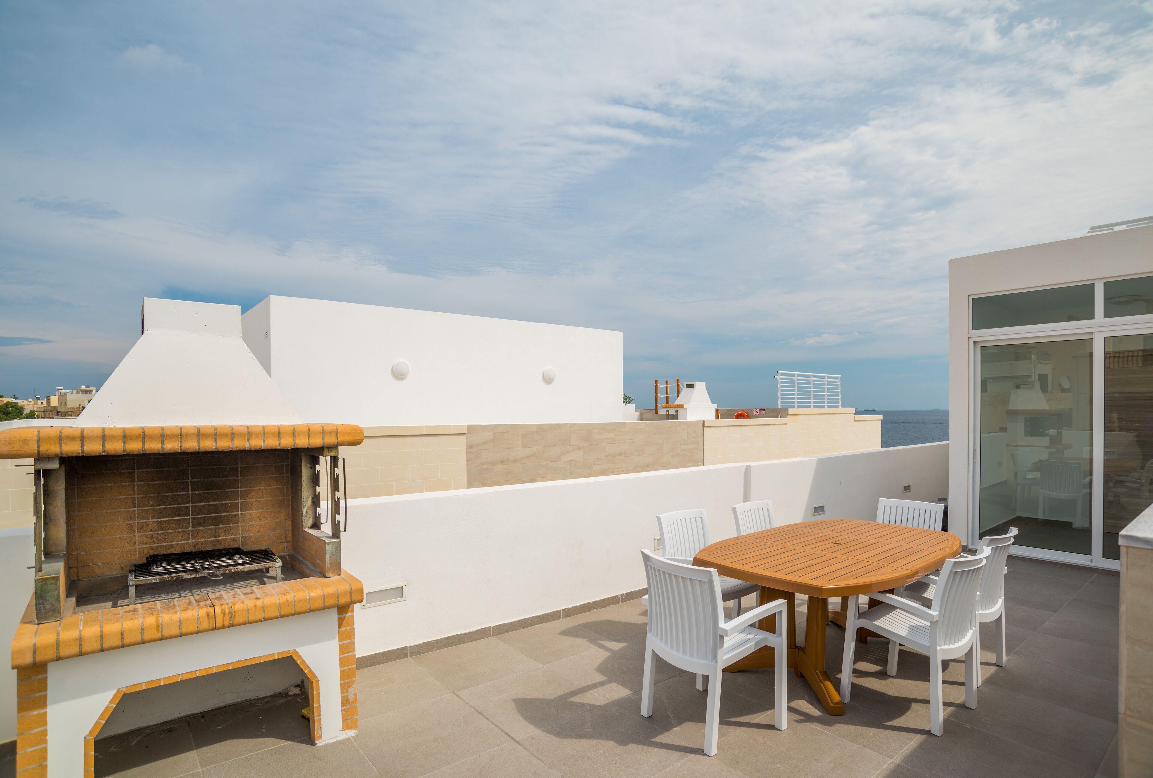 Une terrasse sur le toit équipée d’un barbecue, d’une table en bois et de chaises blanches.