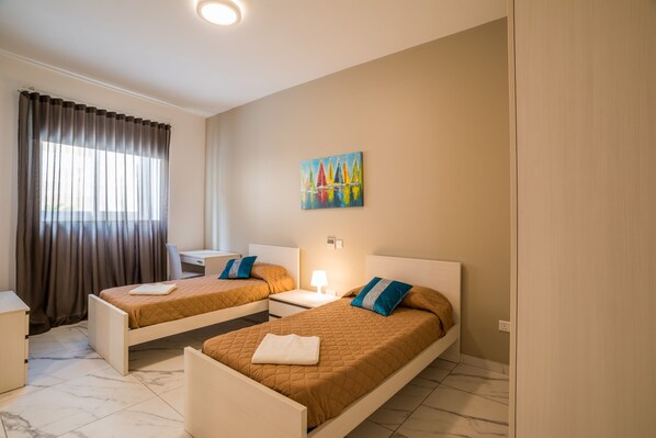 Habitación de hotel con dos camas individuales, un escritorio, una silla y un cuadro en la pared.