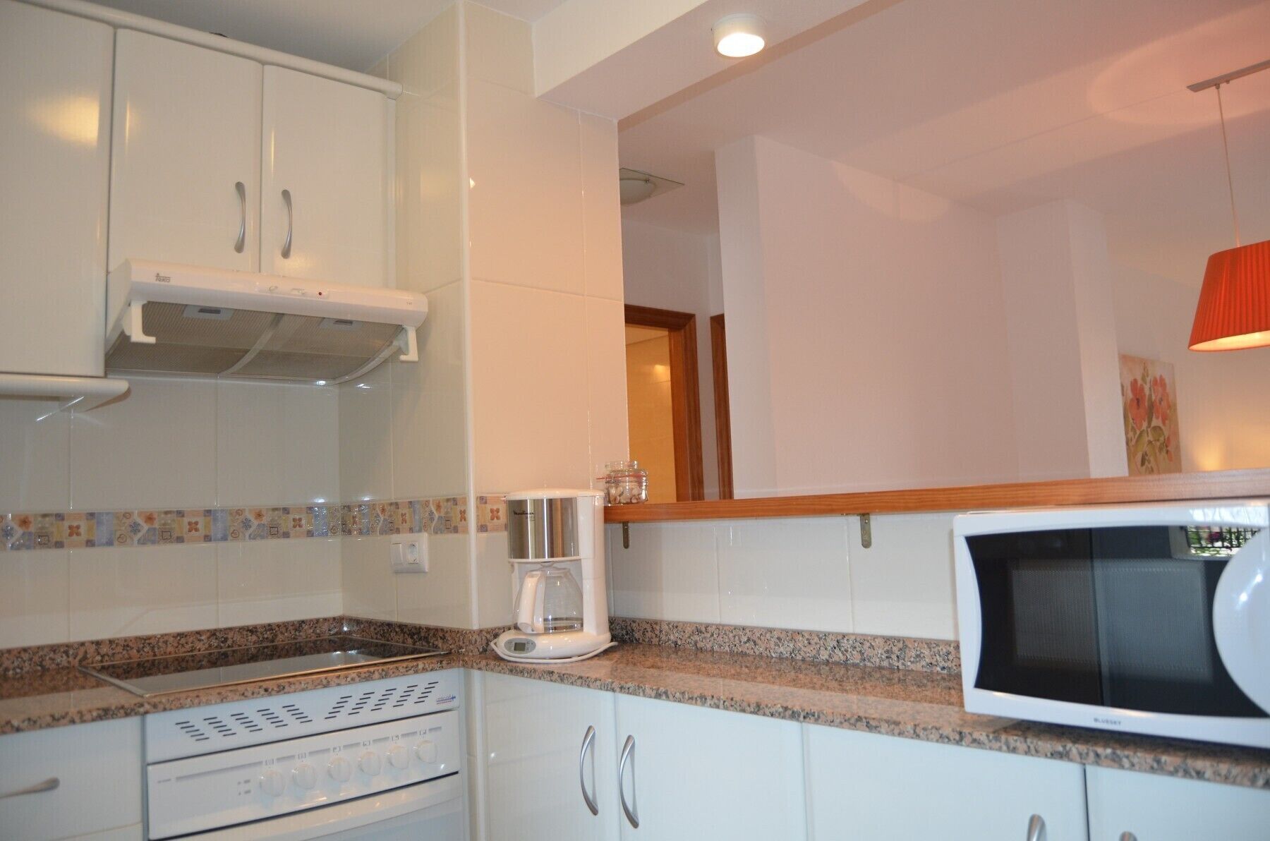 A kitchen with white cabinets, a microwave, a coffee maker, and a stove.