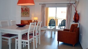 Ein Essbereich mit einem weißen Tisch und Stühlen, einem roten Sofa und einer großen, orangefarbenen Pendelleuchte.