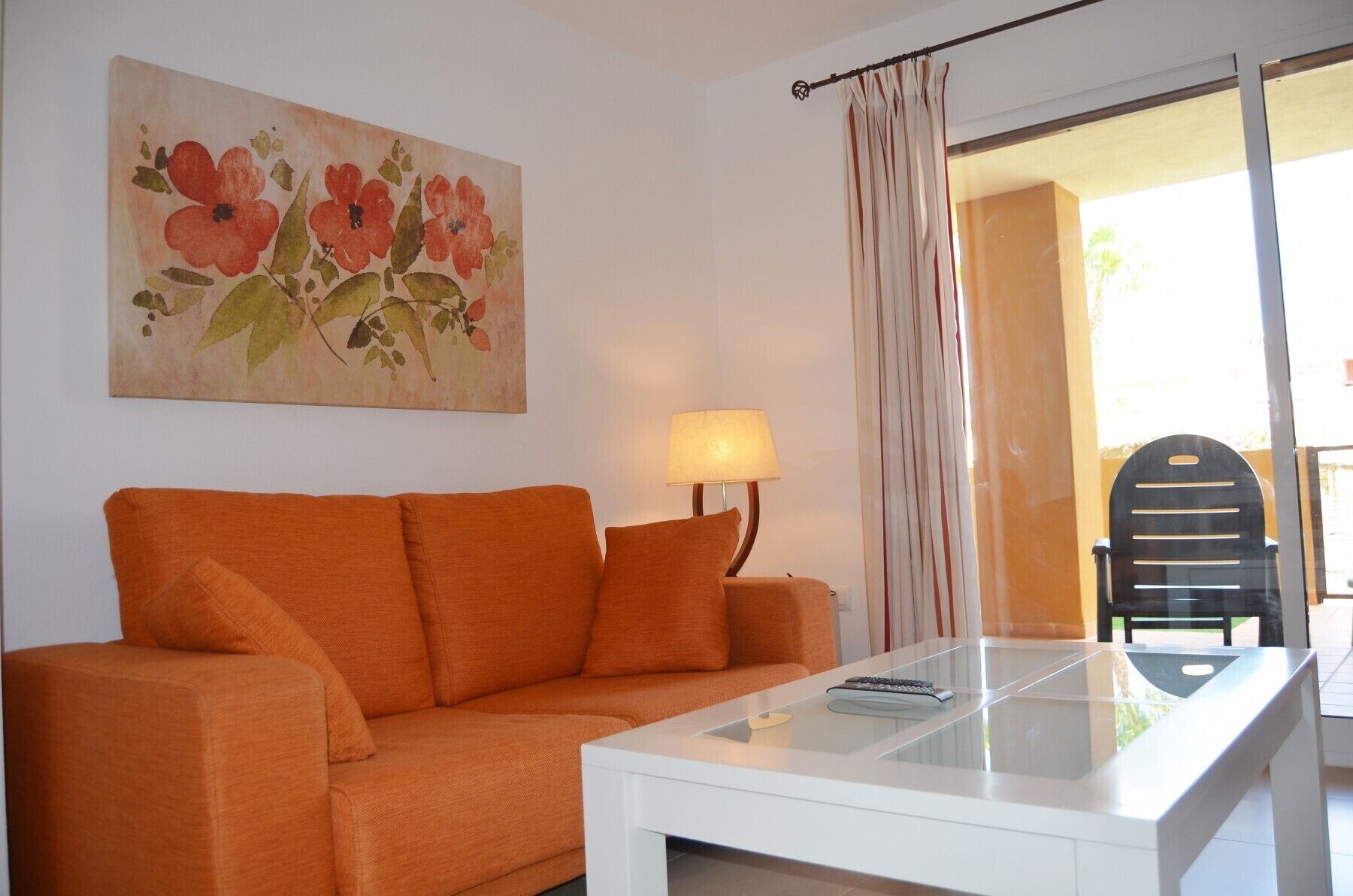 A room with an orange sofa, a white coffee table, a lamp, and a painting of flowers on the wall.
