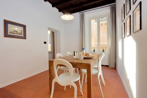 A dining area with a wooden table, white chairs, a hanging light fixture, and a window with curtains.