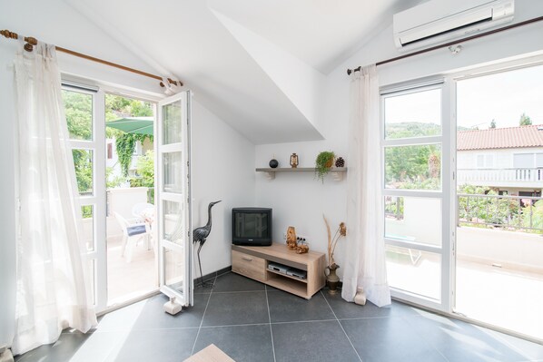 A bright living room with a TV, shelves with plants, and a view of the outdoors.