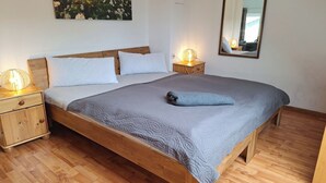 Ein hölzernes Bett mit grauer Steude, zwei Nachttische mit Lampen, ein wandmontierter Spiegel und ein Blumenbild.