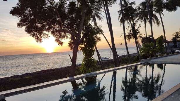 A pool with a view of the sunset over the ocean, surrounded by palm trees. - Bali Apnea Club - Hostel (Kubu)