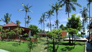 A tropical resort with palm trees, a red-roofed building, and a clear blue sky. - Bali Apnea Club - Hostel (Kubu)