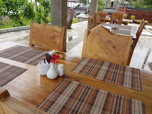 A wooden dining table with a vase of flowers, salt and pepper shakers, and a placemat. - Bali Apnea Club - Hostel (Kubu)